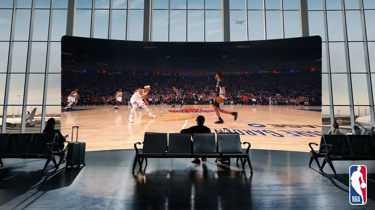 Persona en una sala de espera de aeropuerto viendo un partido de la NBA en una pantalla curva virtual